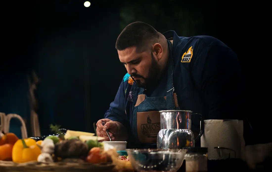 Parrillero frente al fuego preparando carne a las brasas, mostrando pasión y técnica en el arte del asado.