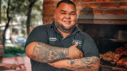 Diego Picagua controlando las brasas con carne asándose lentamente, representando técnica, paciencia y pasión por el fuego lento.