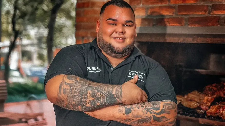 Diego Picagua controlando las brasas con carne asándose lentamente, representando técnica, paciencia y pasión por el fuego lento.