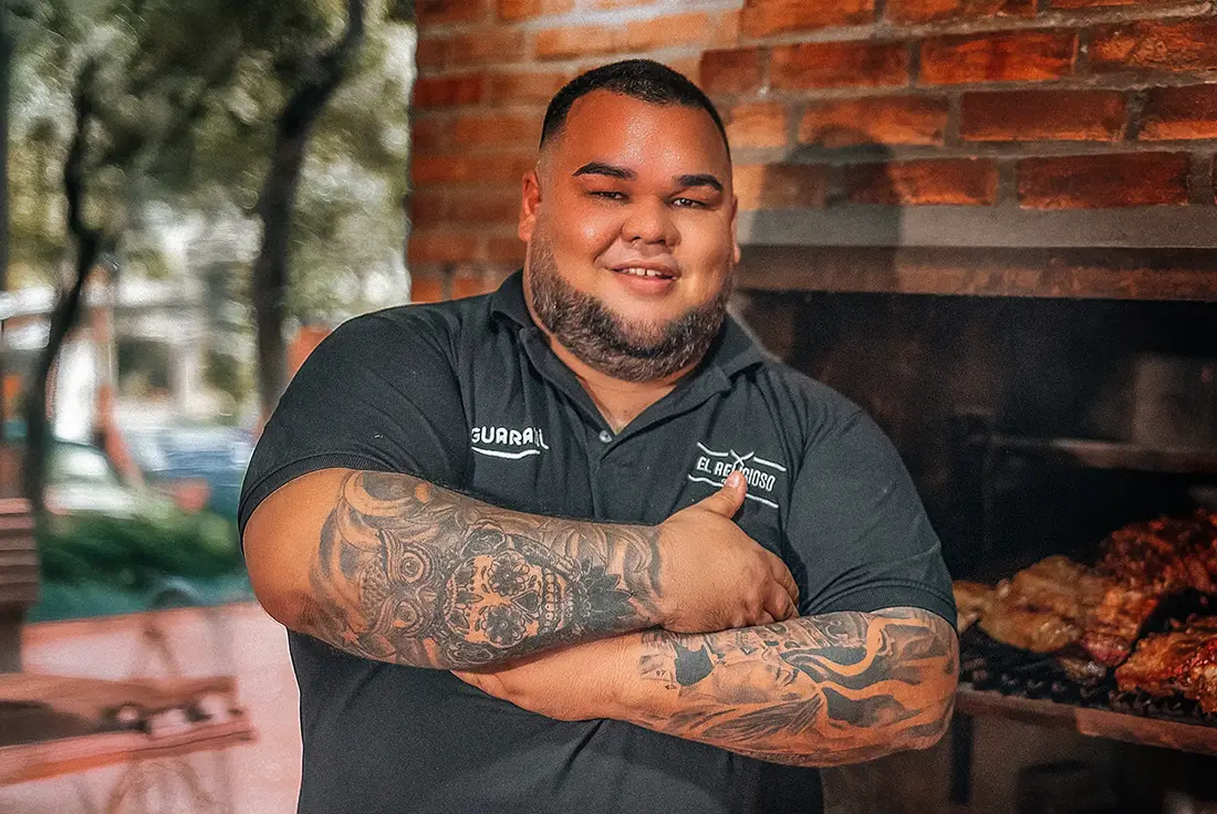 Diego Picagua controlando las brasas con carne asándose lentamente, representando técnica, paciencia y pasión por el fuego lento.